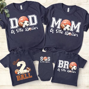 May include: Navy blue family matching t-shirts with sports-themed graphics. Designs include "DAD", "MOM", "BR", and "SS" with sports balls. One shirt says "Born 2 Ball".