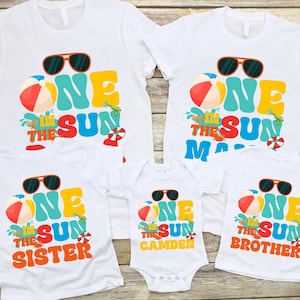 May include: White t-shirts with a colorful "One in the Sun" design, featuring sunglasses, a beach ball, and the words "Sister", "Mom", "Brother", and "Camden". The shirts are perfect for a family vacation or a summer event.
