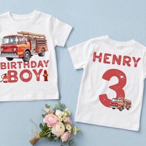 May include: White t-shirts with a red fire truck design. One shirt says "Birthday Boy" with a fire hydrant and fire extinguisher graphic. The other shirt has the name "Henry" and the number "3" with a fire truck graphic.