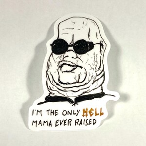 May include: A white sticker featuring a black and white illustration of a person wearing sunglasses. The text on the sticker reads "I'M THE ONLY HELL MAMA EVER RAISED" with the word "HELL" in gold.