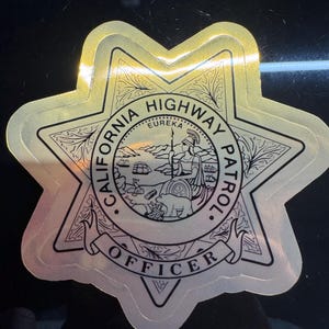 Op de afbeelding: Een goud-zilveren sticker van een California Highway Patrol officier badge. De badge is stervormig met de woorden "California Highway Patrol" en "Officer" in een cirkelvormig ontwerp. Het midden toont een gedetailleerde illustratie van een kustlandschap.