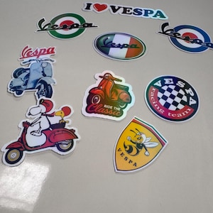 Pode incluir: Uma coleção de autocolantes com o tema Vespa. Inclui o logótipo Vespa, ilustrações de scooters e frases como "I ❤️ Vespa" e "Ride the Classic". Os autocolantes apresentam uma variedade de cores e estilos.