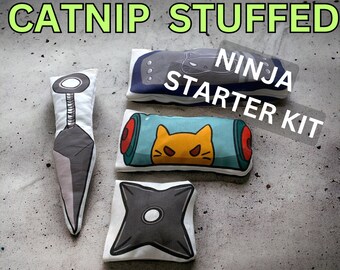 May include: A set of four catnip-stuffed toys shaped like ninja weapons. The toys are white with colorful cartoon images of ninja weapons and a cat. The set includes a kunai, a shuriken, a scroll, and a headband. The toys are labeled "Catnip Stuffed Ninja Starter Kit".