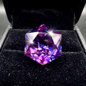 May include: A multi-faceted gemstone in shades of purple and blue, displayed in a black velvet box. The gem's geometric design reflects light, creating a sparkling effect. The overall presentation highlights the gem's beauty and intricate cut.