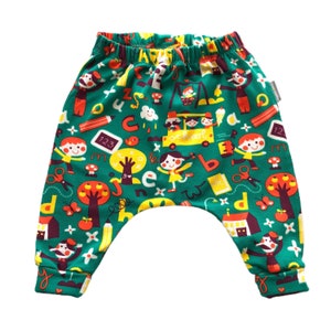 Op de afbeelding: Groene, gele en rode baby harem broek met een schoolthema. De broek heeft een bus, letters, cijfers en kinderen.
