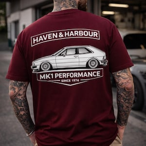 Könnte beinhalten: Burgunderfarbenes T-Shirt mit einer weißen Grafik eines Oldtimers und dem Text "HAVEN & HARBOUR" über dem Auto und "MK1 PERFORMANCE SINCE 1974" darunter. Das Shirt hat einen Rundhalsausschnitt und kurze Ärmel.