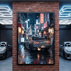Könnte beinhalten: Gerahmter Druck eines grauen Sportwagens, der durch eine nasse, neonbeleuchtete Straße in Japan fährt. Das Bild zeigt japanische Beschilderung und Laternen, mit einer Backsteinmauer und zwei weiteren Autos auf beiden Seiten.