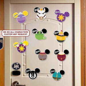 May include: A collection of colorful character-themed decals in the shape of Mickey Mouse ears, affixed to a white door. The decals feature various designs, including a frog, a horse, and a sun. Text on the door reads "WE DO ALL CHARACTERS CUSTOM ANY REQUEST."