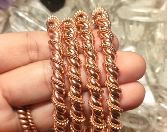 Könnte beinhalten: Vier kupferfarbene Metallarmreifen mit einem gedrehten Seildesign. Jeder Armreif hat eine polierte, reflektierende Oberfläche mit einem sich wiederholenden Spiralmuster. Die Armbänder sind vertikal angeordnet und zeigen die Textur.