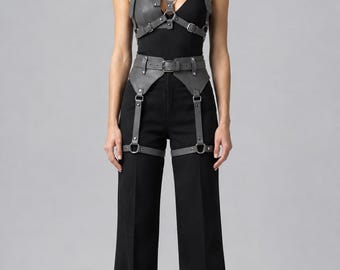 May include: A grey leather harness set featuring a chest piece with adjustable straps, metal rings, and buckles, paired with a matching waist belt that includes integrated leg straps and hardware, worn over a black sleeveless top and black trousers.