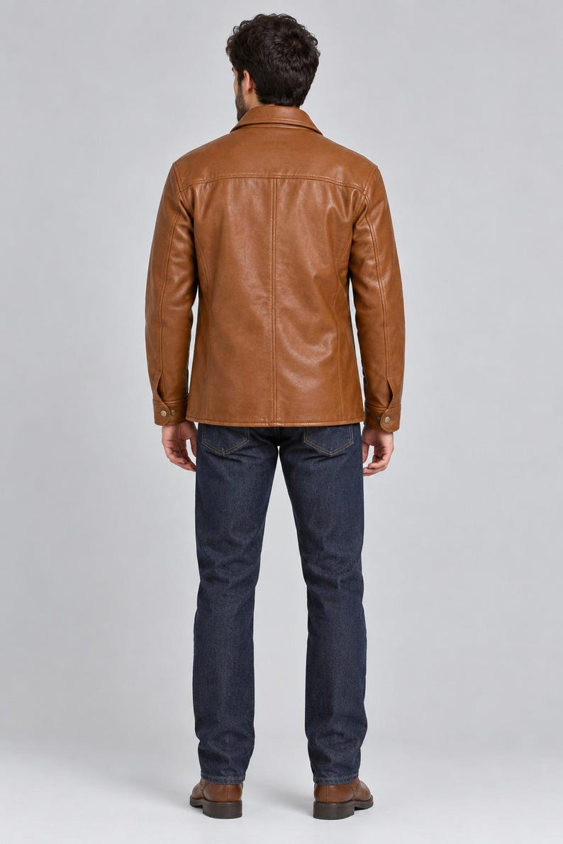 May include: A tan leather jacket with a pointed collar, long sleeves with buttoned cuffs, and vertical seam detailing on the back, paired with dark blue denim jeans and brown leather shoes, viewed from the back against a plain light gray background.