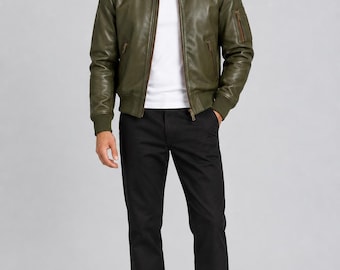 May include: An olive green leather bomber jacket with a ribbed collar, cuffs, and hem, featuring a front zipper closure and a zippered utility pocket on the left sleeve, worn over a plain white t-shirt with black trousers and white sneakers.