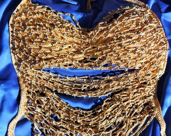 May include: A gold-colored, handmade halter top with intricate crochet detailing. The top features multiple strands of gold thread, adorned with small, silver-colored beads. The halter top is displayed on a blue fabric background.