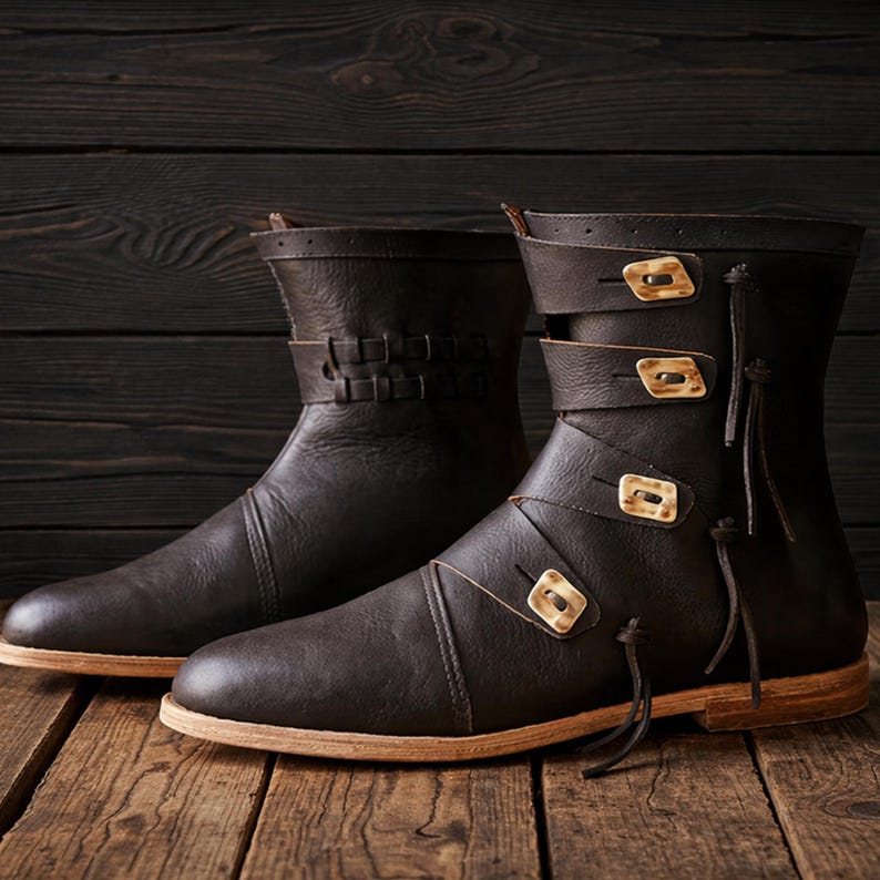 May include: A pair of brown leather boots with decorative buckles and straps. The boots have a mid-calf height and a light-colored sole. The leather appears to be distressed, giving them a vintage look. The boots are displayed on a wooden surface.