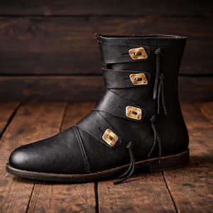 May include: Black leather boot with three straps and gold-colored buckles. The boot has a rounded toe and a short shaft, with decorative tassels on the side. The boot is set against a wooden background.