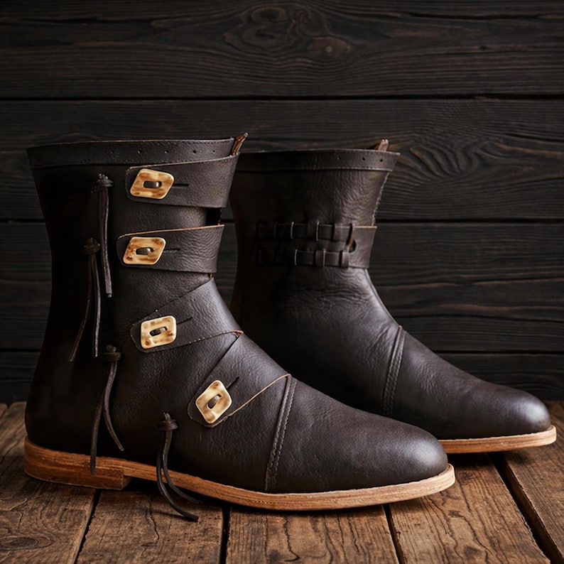 May include: A pair of dark brown leather boots with decorative straps and buckles. The boots have a mid-calf height and a light-colored sole. The buckles are a light tan color. The boots are displayed on a dark wooden surface.