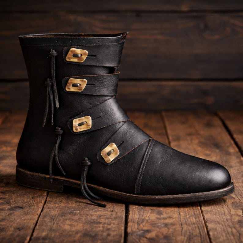 May include: Black leather boot with three straps and decorative gold-colored square buckles. The boot has a rounded toe and a short shaft, with decorative leather ties on the side. The boot is set on a wooden surface.