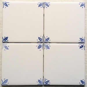 May include: Four square white ceramic tiles arranged together. Each tile has a blue floral corner design. The tiles are on a neutral linen surface. The overall design is simple and elegant, suitable for home decor.