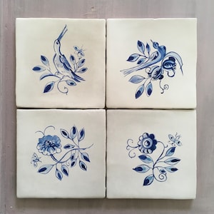 May include: Four square ceramic tiles with hand-painted blue and white designs. Each tile features a different illustration of birds, flowers, and foliage. The tiles are arranged in a 2x2 grid.