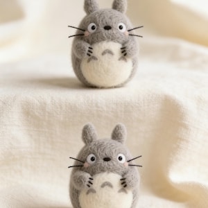 Puede incluir: Dos figuras de Totoro de fieltro gris con vientres blancos y bigotes negros. Las figuras tienen orejas peque&ntilde;as y est&aacute;n colocadas sobre una tela color crema. Las figuras est&aacute;n hechas a mano y probablemente forman parte de una colecci&oacute;n o exhibici&oacute;n.