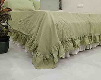 May include: A sage green bedspread featuring a ruffled edge and a white ruffled bed skirt underneath. The bedspread covers a bed with a tufted white headboard, and a silver laptop is placed on the surface of the bed near the headboard.
