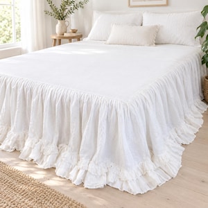 May include: A white bedspread featuring a long, gathered ruffle skirt that extends to the floor. The bedding set includes two matching white pillows and a smaller rectangular accent pillow, all in a solid, textured white fabric.