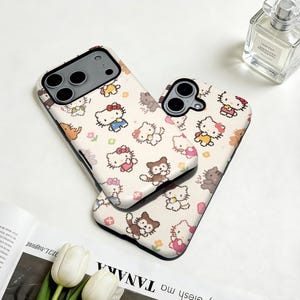 May include: Two phone cases with a repeating pattern of cartoon cats and other characters in various outfits and poses. The cases are white with black edges. The design includes characters with red, pink, yellow, and blue clothing. The cases are on a white surface.