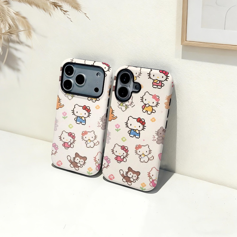 May include: Two phone cases with a repeating pattern of pixelated Hello Kitty characters in various outfits and poses. The cases are white with a black border and have cutouts for the camera and buttons.