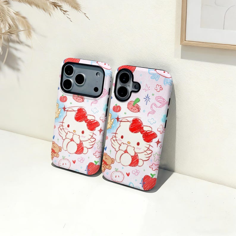 Puede incluir: Dos fundas para tel&eacute;fono con fondo blanco y un patr&oacute;n repetido de manzanas rojas, ositos de peluche y personajes de Hello Kitty con lazos rojos. Las fundas tienen recortes negros para la c&aacute;mara.