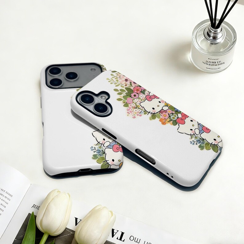 Puede incluir: Fundas blancas para tel&eacute;fono con dise&ntilde;o floral y personajes de Hello Kitty. Las fundas tienen un acabado brillante y un recorte negro para la c&aacute;mara. El dise&ntilde;o incluye elementos florales rosas, blancos y verdes.