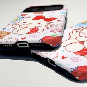 Puede incluir: Dos fundas blancas para tel&eacute;fono con un dise&ntilde;o de dibujos animados colorido. Las fundas presentan un personaje lindo con un lazo rojo, fresas, nubes y corazones. Las fundas tienen bordes negros y est&aacute;n sobre una superficie blanca.