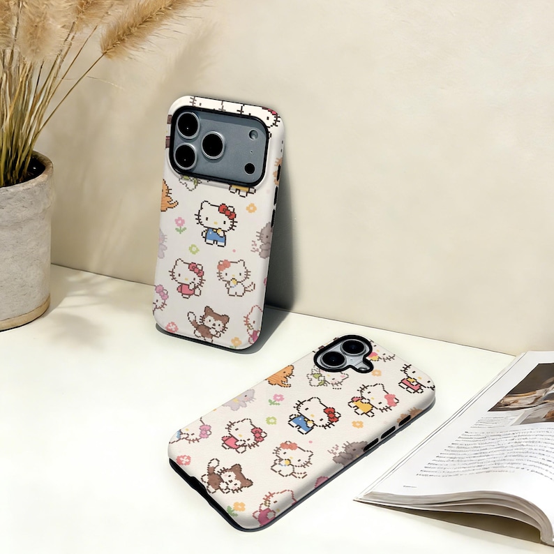 May include: Two white phone cases with a repeating pattern of Hello Kitty characters in various outfits. The cases have a black border and are on a white surface. One case is upright, and the other is lying down.