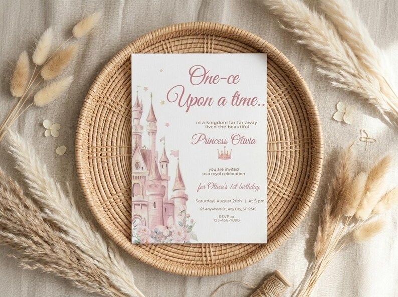 May include: A princess-themed invitation card with the text "One-ce Upon a time..." and "Princess Olivia". The card features a pink castle illustration and floral accents. The invitation is set on a woven tray with decorative dried plants.
