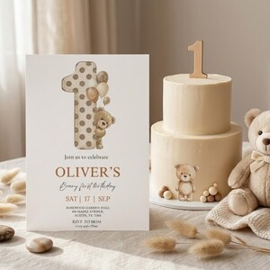 Pode incluir: Cena de anivers&aacute;rio com um bolo de dois andares, um topo de bolo com o n&uacute;mero um, um ursinho de pel&uacute;cia e um convite. O convite diz "OLIVER'S Beary first birthday" com a data e o local.