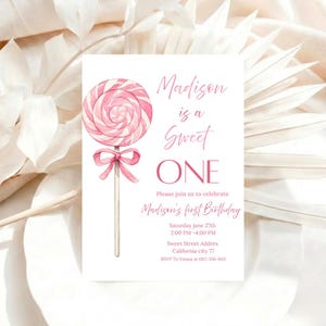 May include: A pink and white lollipop illustration adorns a white invitation card. The text reads "Madison is a Sweet ONE" and invites guests to Madison's first birthday. Details include the date, time, and location.