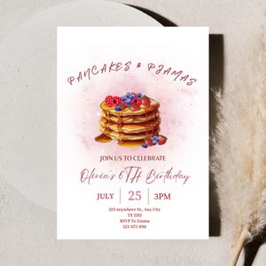 Op de afbeelding: Witte uitnodigingskaart met de tekst "PANCAKES & PJAMAS" en een stapel pannenkoeken met siroop, blauwe bessen en aardbeien. De uitnodiging is voor Olivia's 6e verjaardag op 25 juli om 15.00 uur.