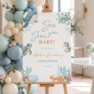 Op de afbeelding: Een welkomstbord voor een babyshower met een zeethema. Het bord toont illustraties van een walvis, octopus, schildpad en zeepaardje. Tekst luidt "Sea you soon BABY!" en "Welcome to Aleshia Beaching BABYSOWER 08.07.20XX". Het bord staat op een houten ezel.