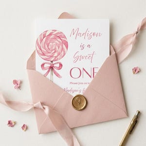May include: A pink invitation card with a watercolor lollipop illustration, inside a matching envelope. The card reads "Madison is a Sweet ONE" with additional text. A gold wax seal and pink ribbon complete the design, perfect for a first birthday.