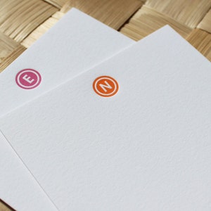 May include: Two white cards with a pink circle containing the letter "E" and an orange circle containing the letter "N".