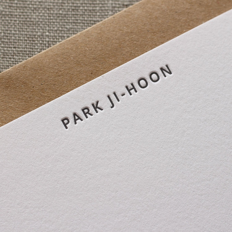 Close up of letterpress stationery with a deep impression into soft cotton paper. The font is a modern, sans serif font.