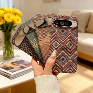 May include: A hand holds several phone cases with various geometric patterns. The cases feature designs in brown, green, and a vibrant mix of red, blue, and yellow. The cases are designed to fit a specific phone model.
