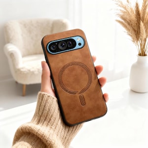 May include: A brown leather phone case with a black border. The case features a circular design on the back and a camera cutout with blue accents. The phone case is held in a person's hand.
