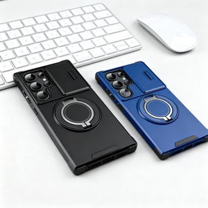 May include: Two phone cases, one black and one blue, with a camera cover and a ring holder. The cases are on a white surface with a keyboard and mouse in the background. The ring holder is silver.