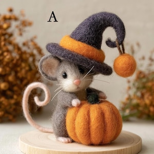 Könnte beinhalten: Eine nadelgefilzte graue Mausfigur mit der Kennzeichnung A, die einen dunkelvioletten Hexenhut mit orangefarbenem Band und einem baumelnden orangefarbenen Bommel trägt. Die Maus hält einen strukturierten orangefarbenen Kürbis und hat einen langen, geringelten hellrosa Schwanz.