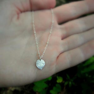 May include: A delicate silver necklace with a small, detailed leaf pendant. The chain is made of tiny silver beads.