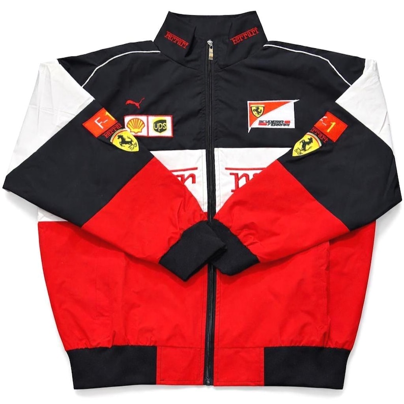 May include: A Ferrari racing jacket in red, black, and white. The jacket features the Ferrari logo, sponsor patches, and the Puma logo. The jacket has a zipper closure and black cuffs and hem.