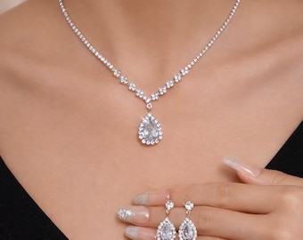 May include: A sparkling silver necklace and matching earrings set. The necklace features a delicate chain with a teardrop pendant. The earrings are teardrop-shaped and dangle. The jewelry is adorned with clear, shimmering stones.