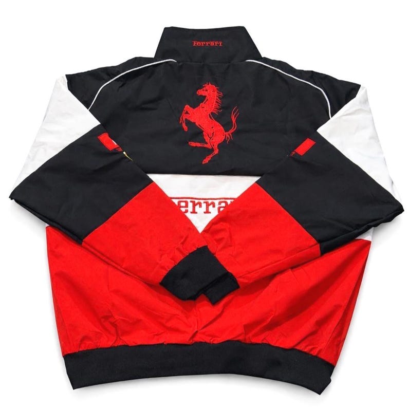 May include: A Ferrari racing jacket in red, black, and white. The jacket features the Ferrari logo and branding on the back and collar. The sleeves are black and white, and the body is red and black.