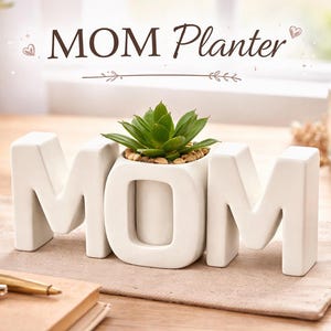 Puede incluir: Una maceta de cerámica blanca con la forma de la palabra "MOM" con una pequeña planta suculenta en su interior. La maceta está sobre un mantel individual beige, con una vela y libros en el fondo. El texto "MOM Planter" está arriba.