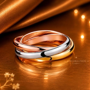 Può includere: Un anello a tre colori composto da tre fasce intrecciate in oro rosa, oro giallo e metallo color argento lucido. Le fasce lisce e arrotondate sono collegate tra loro per formare un unico gioiello che riporta il testo ATELIER.LUXEIN.